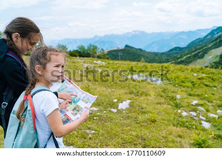 Children hiking on beautiful summer day in alps mountains Austria resting on rock. Kids look at map mountain peaks in valley. Active family vacation leisure with kids.Outdoor fun and healthy activity