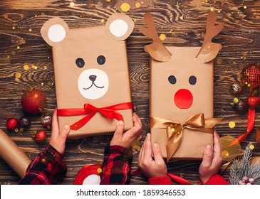 Children Hold Creatively Wrapped Christmas Gifts In The Shape Of A Teddy Bear And A Deer. New Year And Christmas Concept. DIY Gift Wrapping