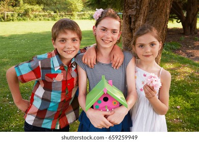 Children Holding Birdhouse In Backyard