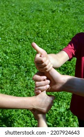 Children Holding Each Other's Thumbs To Rhyme Before A Game, Kids Playing In Summer Camp, Vacations, Green Grass Background, No Faces