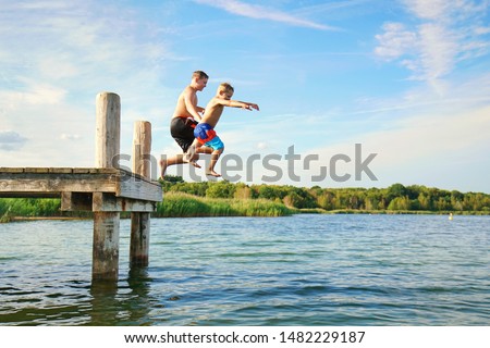 children jumping from wooden jetty into the lake - refreshing on hot summer
