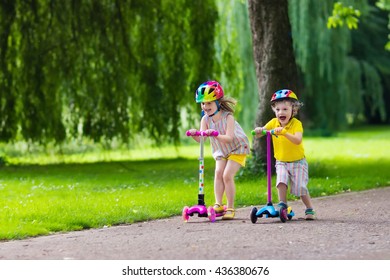 Children learn to ride scooter in a park on sunny summer day. Preschooler boy and girl in safety helmet riding a roller. Kids play outdoors with scooters. Active leisure and outdoor sport for child. - Powered by Shutterstock