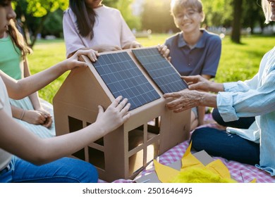 Children learning about renewable energy and solar panels during sustainable education class outdoors, using cardboard model of house wit solar panel on roof. - Powered by Shutterstock