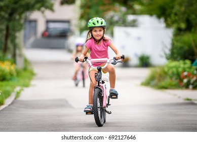 Children learning to drive a bicycle on a driveway outside. Little girls riding bikes on asphalt road in the city wearing helmets as protective gear.