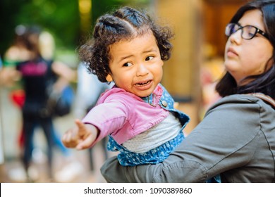 Children Learning And Family Real Life Concept. Candid Moment Of Latino American Mother And Dark Skinned Hispanic Toddler Daughter Crying And Pointing Somewhere During A Walk Outdoors.