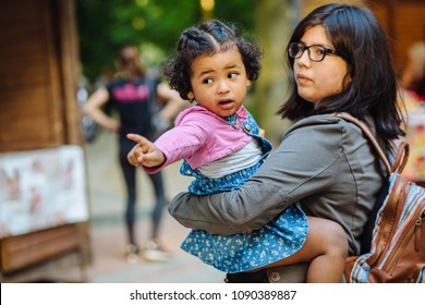 Children Learning And Family Real Life Concept. Candid Moment Of Latino American Mother And Dark Skinned Hispanic Toddler Daughter Crying And Pointing Somewhere During A Walk Outdoors.