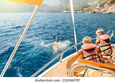 Children in life jackets sit on boat watching mother swimming in sea against coast of Marmaris. Woman with toddler and preschooler enjoy vacation in Turkey - Shutterstock ID 2150369787