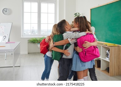 Children meet each other after long vacation. Group of little school friends hugging tightly during meeting in elementary school classroom. Boys and girls with backpacks hug when they come to school.