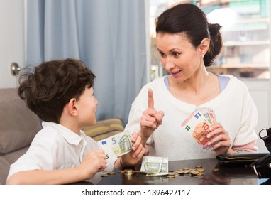 Children And Money Concept. Woman Admonishing Teen Boy While Giving Him Money At Home