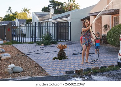 Children, mother and hose for car washing, cleaning and learning responsibility and development outdoor. Child or kid and mom for sibling, childhood and cute for water or fun on holiday for weekend - Powered by Shutterstock