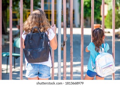 Children Near Gate Of Closed School. Little Girls Outside Closed School Grounds.