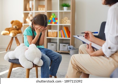 Children Need Help. Bullied Little Schoolgirl Crying In Psychologist's Office Unable To Control Emotions, Sharing Problems And Traumas. Professional Psychotherapist Talking To Distressed Bully Victim