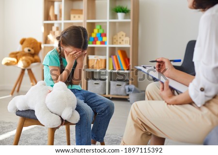 Children need help. Bullied little schoolgirl crying in psychologist's office unable to control emotions, sharing problems and traumas. Professional psychotherapist talking to distressed bully victim