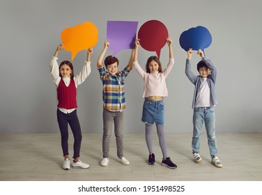 Children Of New Generation Voice Out Opinions. Group Of Cute Junior Kids Holding Up Multicolored Clean Paper Speech Bubbles. Happy Elementary School Boys And Girls With Text Bubbles Standing In Studio