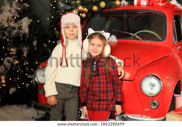 Children on the background of a red car with New\
Year\'s gifts. Boy and girl driving a car at Christmas. Lots of\
gifts on the Christmas\
car