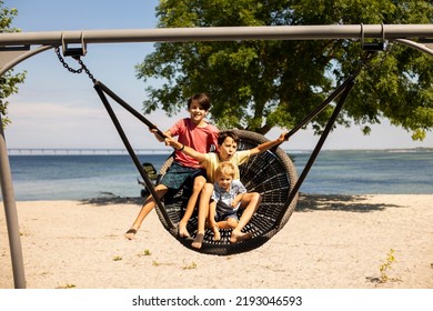 Children On Beach Swing. Kid Swinging In Malmo, Sweden, Travel With Young Children. Summer Family Vacation With Kids Playing  On Sea Shore