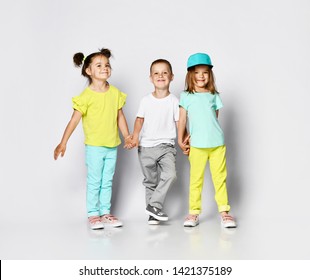 Children On A Light Background: Full Body Shot Of Three Children In Bright Clothes, Two Girls And One Boy. Triplets, Brother And Sisters. Laughing And Screaming Loud Have Fun In The Studio