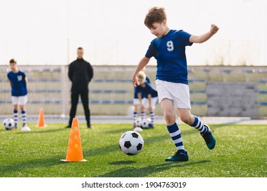 Children on summer soccer training camp. Group of young boys on football outdoor practice session. Happy boys running after ball towards training cone. Coach trainer, soccer team players in background - Powered by Shutterstock