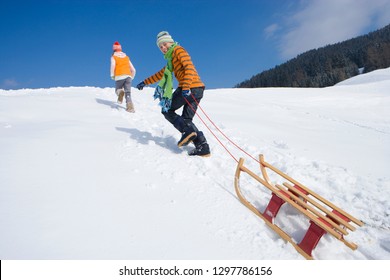 Children on winter vacation pulling sled up snowy mountain smiling at camera