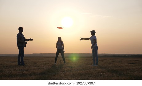 Children And Parents, Family Play In Field. Happy Family, Dad, Mom And Daughter Are Playing, Throwing Flying Red Disc To Each Other In Park. Carefree Young People Have Fun Together. Sports And Youth.