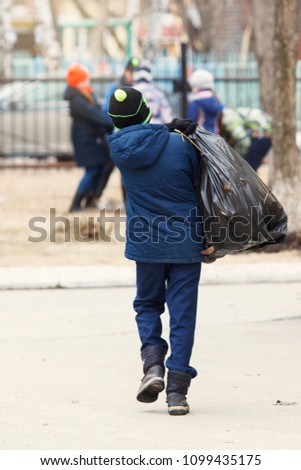 Children picking up trash in the schoolyard. The concept of environmental protection. Schoolboys carry black garbage bags.