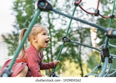 Children play and climb outdoors on a sunny summer day. Nice kid girl on a swing nest in a preschool sports complex. - Powered by Shutterstock