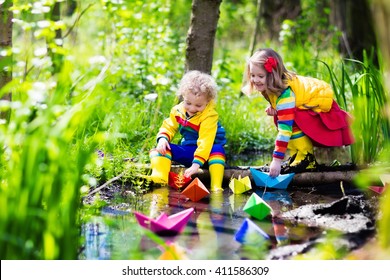 Children Play With Colorful Paper Boats In A Small River On A Sunny Spring Day. Kids Playing Exploring The Nature. Brother And Sister Having Fun At A Forest Stream. Boy And Girl With Toy Boat And Ship