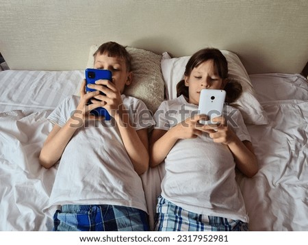 Children play at home with smartphones lying in bed. Children phone addictions