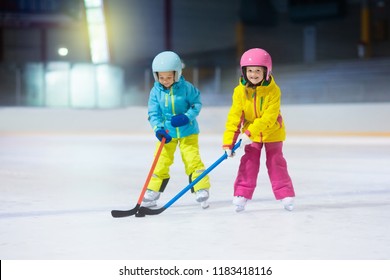 Children Play Ice Hockey On Indoor Rink. Healthy Winter Sport For Kids. Boy And Girl With Hockey Sticks Hitting Puck. Child Skating. Little Kid On Sports Training After School. Snow And Ice Fun.