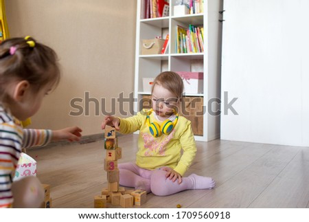 children play on the floor in the children's room. Two girls collect wooden cubes