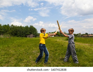 Children Play Outdoors In The Park And Fight With Wooden Swords.