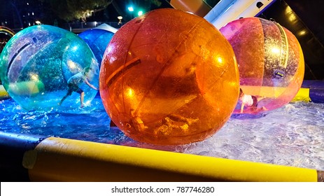 Children Play In The Pool Inside Large
Balls. Favourite Children's Water Activities - Zorbing In The Swimming Pool. Aquazorbing. Kids Playing Together And Having Fun. Colorful Balloons. Night Light