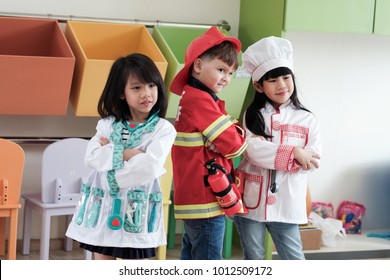 Children Play Role, Caucasian Boy And Asian Girls Playing As Fireman, Doctor And Cook Occupation With Tool Toys In Kindergarten Classroom, Children In Role Occupation, Education Concept