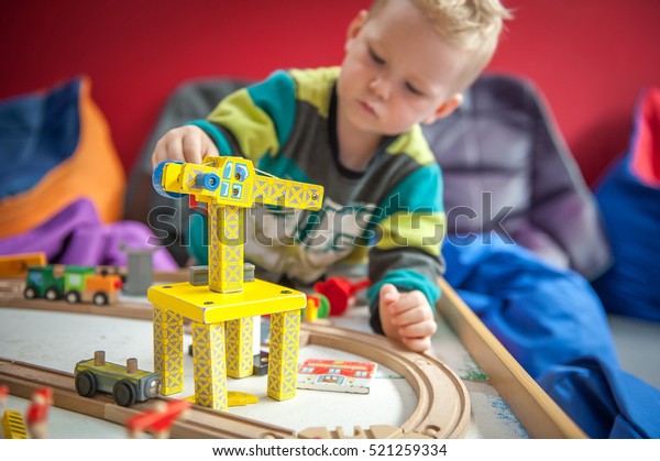 Children play with wooden toy, build toy railroad at\
home or daycare. Toddler boy play with crane, train and cars.\
Educational toys for preschool and kindergarten child. Cushioned\
furniture, chair bag