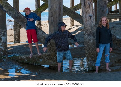 Children playfully pose for camera under a pier at Siletz Bay Park in Lincon City on the Oregon Coast