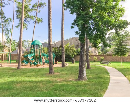 Children playground activities in residential area, pathway surrounded by pine trees, grass lawn at sunset in Humble, Texas, US. Kids run, slide, swing on modern playground. Urban neighborhood concept