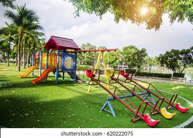  Children playground on yard activities in public park surrounded by green trees at sunlight morning. Children run, slide, swing,seesaw on modern playground. Urban neighborhood childhood concept. - Powered by Shutterstock