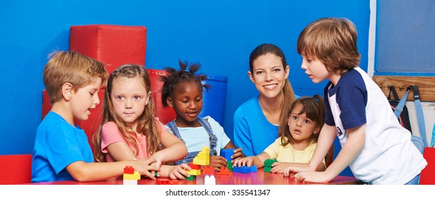 Children Playing With Building Bricks In Child Care With Nursery Teacher