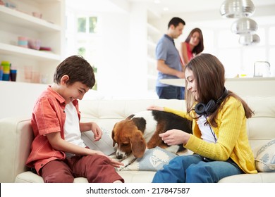 Children Playing With Dog On Sofa As Parents Make Meal - Powered by Shutterstock