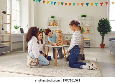 Children playing with educational toys in cozy after-school centre. Group of quiet diverse 8-10-year-old kids busy with interesting wood block tower stacking board game during birthday party at home
