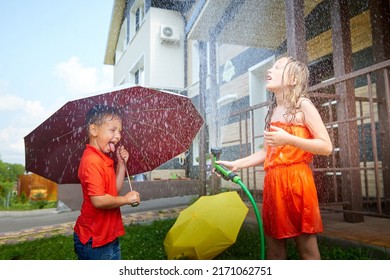 Children Playing With Garden Sprinkler. Brother And Sister Running And Jumping. Summer Outdoor Water Fun In Backyard. Boy And Girl Play With Hose Watering Grass. Kids Run And Splash On Hot Sunny Day