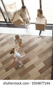 Children Playing Having Fun Exploring Luxury Living Room While Parents Holding Boxes Entering House On Moving Day, Happy Family With Kids Son And Daughter Relocating Into New Home, Vertical Top View