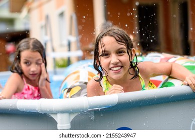 Children playing in home swimming pool in the summer. Girls are enjoying summer vacation in the back or front yard swimming pool. Kids splashing water, smiling and having fun.
