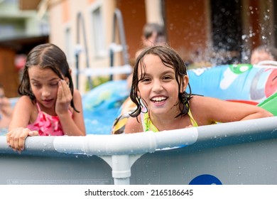 Children Playing In Home Swimming Pool In The Summer. Girls Are Enjoying Summer Vacation In The Back Or Front Yard Swimming Pool. Kids Splashing Water, Smiling And Having Fun.