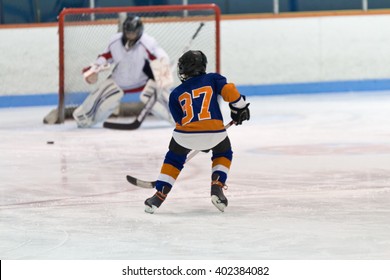 Children Playing Ice Hockey In An Arena With Player Skating Towards Goaltender