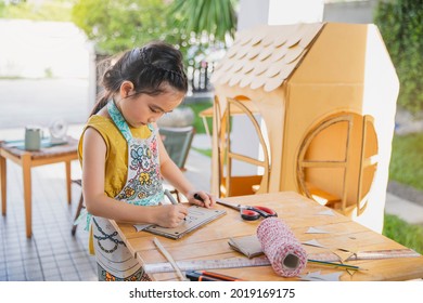 Children playing with little paper cafe at home. Asian little child girl with her cardboard house. children were painting,drawing on the house made of paper. STEAM education