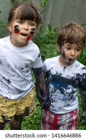 Children Playing In Mud, Dirty Cloth, Messy Face And Hands In Mud. Stains On Clothes. Dirty Cloth, Washing Laundry Concept.