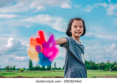 Children playing rainbow pinwheel or windmill on blue sky and clouds background of beautiful nature, kids smiling and playful pinwheel on windy, happ Asian child joy toys for relaxing time to funny
