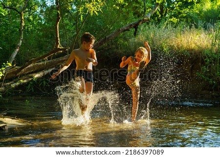 children playing in the river. A girl and boy raises her hands up in the water and splashes water drops