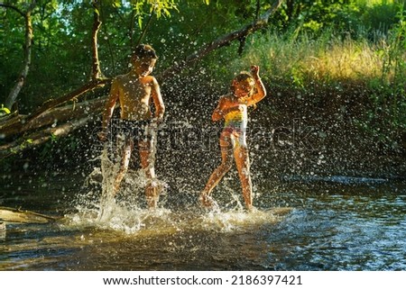 children playing in the river. A girl and boy raises her hands up in the water and splashes water drops
